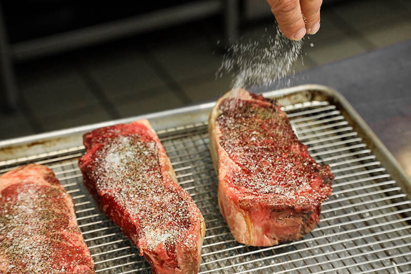 steaks being seasoned with salt.