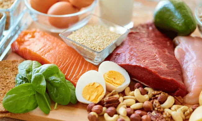 A variety of fresh protein-rich ingredients like fish, beef, chicken, eggs, nuts, spinach, and grains displayed together.