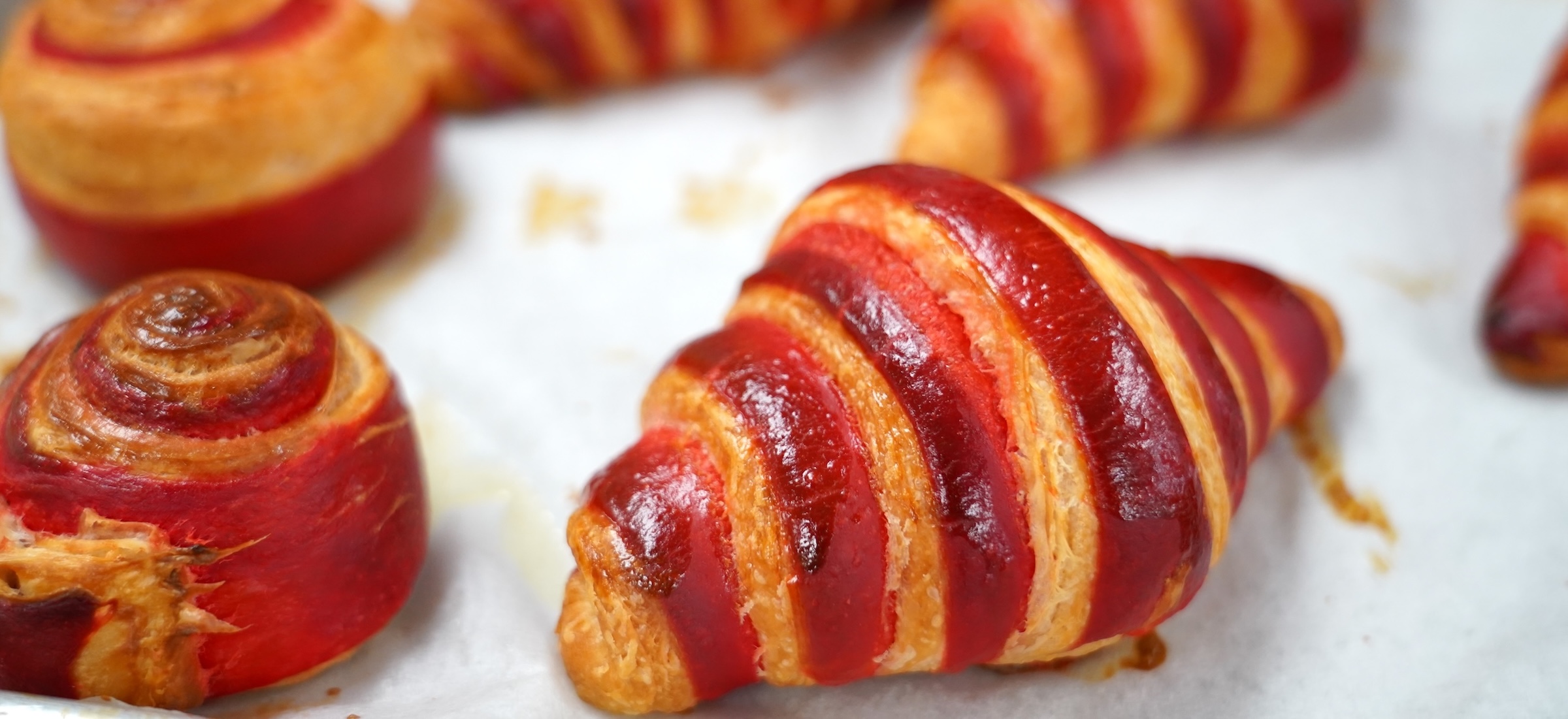 Red and golden brown striped croissants sit on a parchment paper lined sheet tray