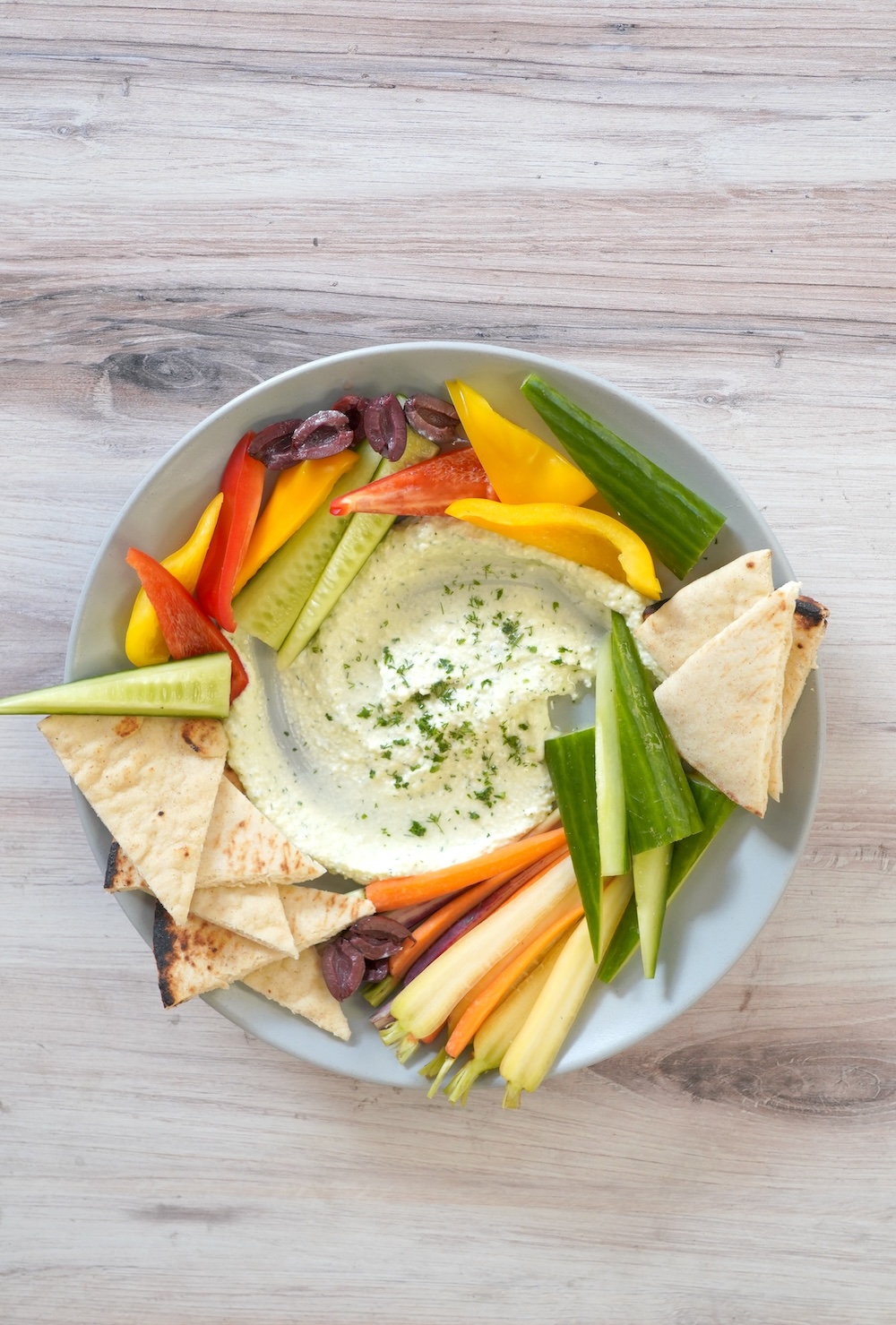 Whipped feta dip on a blue plate surrounded by vegetables