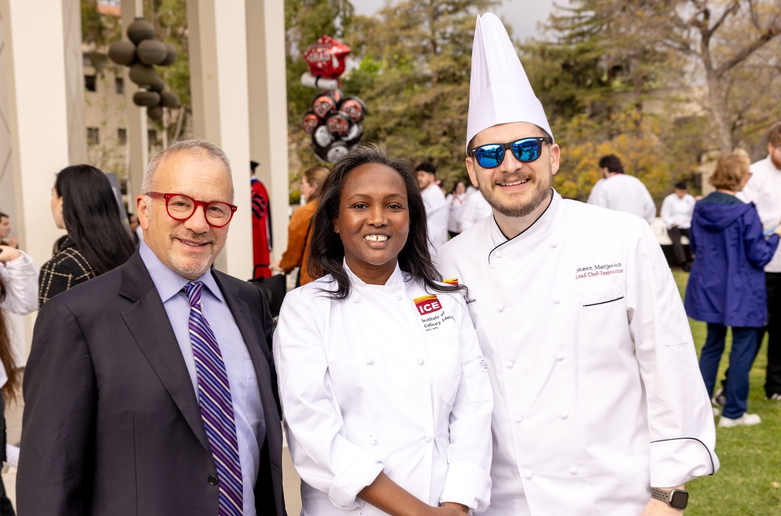Culinary school online student Meymuna Hussein smiles with ICE owner and chairman Rick Smilow and Chef Shawn Matijevich