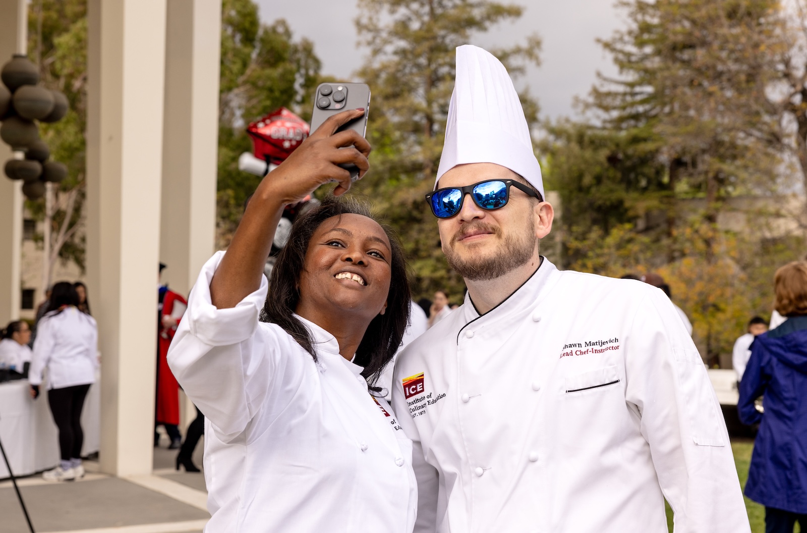 ICE online culinary school graduate Meymuna Hussein-Cattan takes a photo with Lead Chef-Instructor Shawn Matijevich at commencement