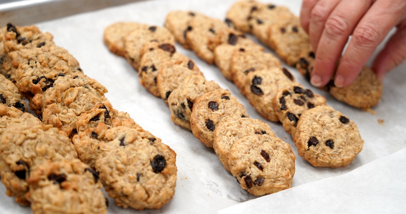 A hand reaches for an oatmeal cookie on a tray