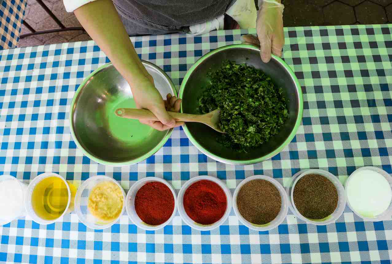 Chef hands mixing herbs in a bowl, spices lined up in a row 