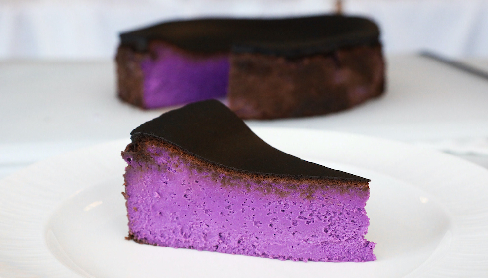 Purple Basque cheesecake slice on a plate, with the rest of the cake in the background