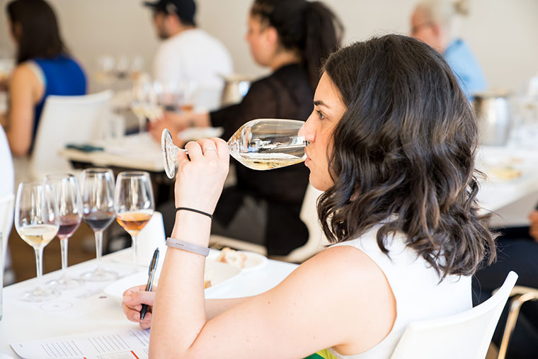 An image of a brown-haired woman sipping white wine from a wine glass