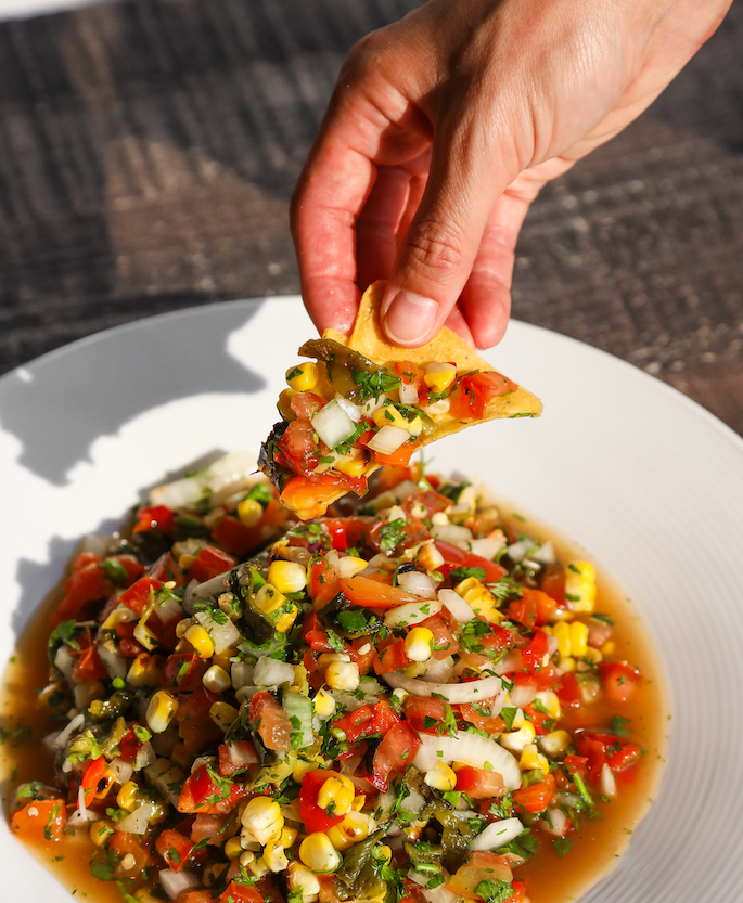 Hand dipping a chip into a corn tomato salsa