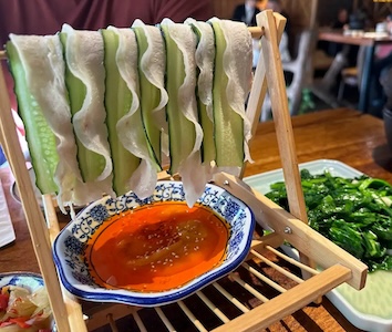 Pork belly and cucumber hanging on a wooden bar over sauce