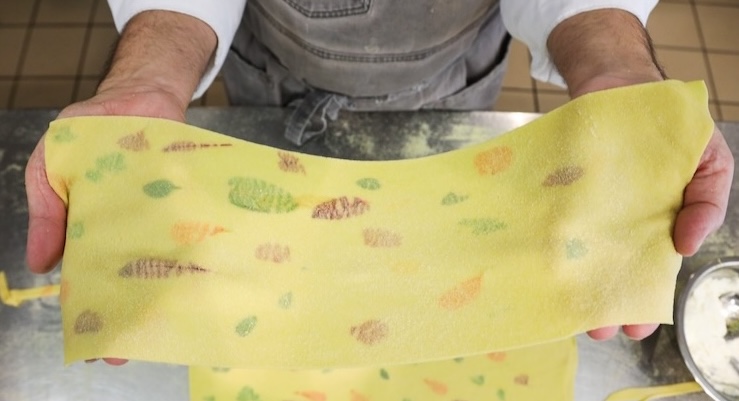 hands holding pasta sheet speckled with herbs and flowers