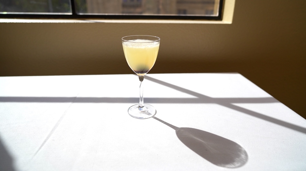 A slight green Corpse Reviver #2 drink in a Nick and Nora glass on a white table