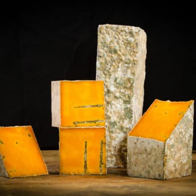 Multiple slabs of red rock cheese, cut open to reveal bright orange cross sections, sit on a wooden table