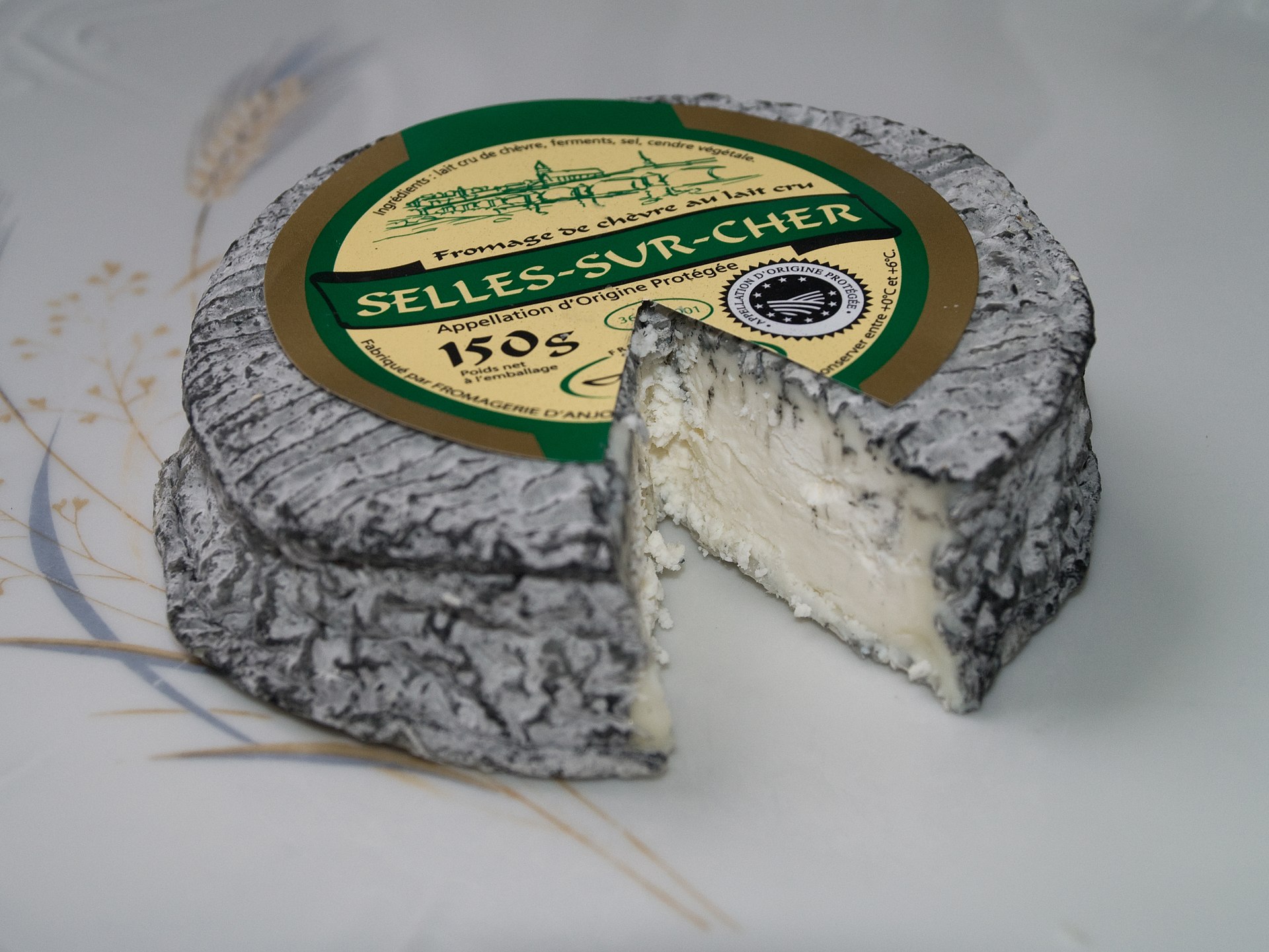 A wheel of Selles Sur Cher cheese with one cut out wedge, with a white interior and a black ashy exterior