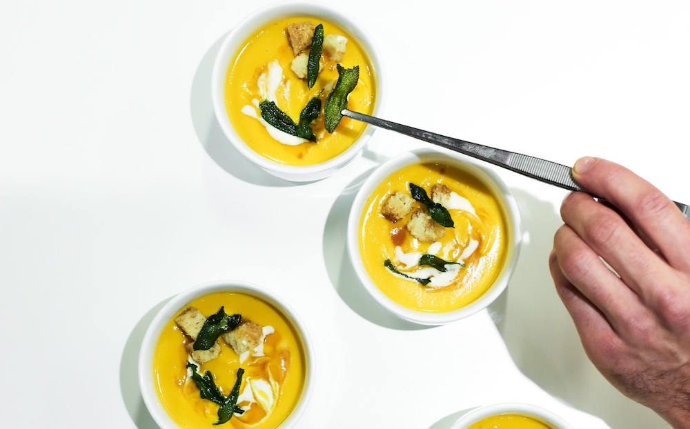 A hands plates yellow sweet potato soup in white ramekins on a white background