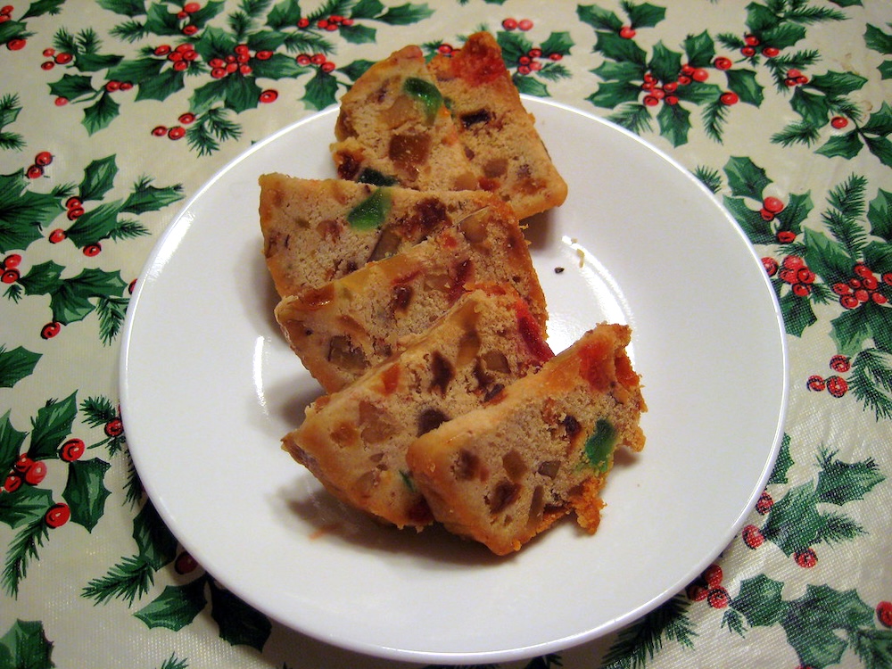 Five slices of fruit cake, dotted with green and red fruit, on a white plate