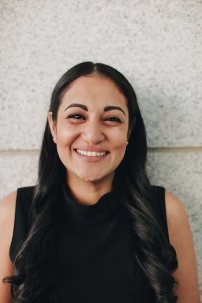 Food writer and restaurant reviewer Mahira Rivers standing and smiling beside a wall smiling wearing black shirt and long black hair 