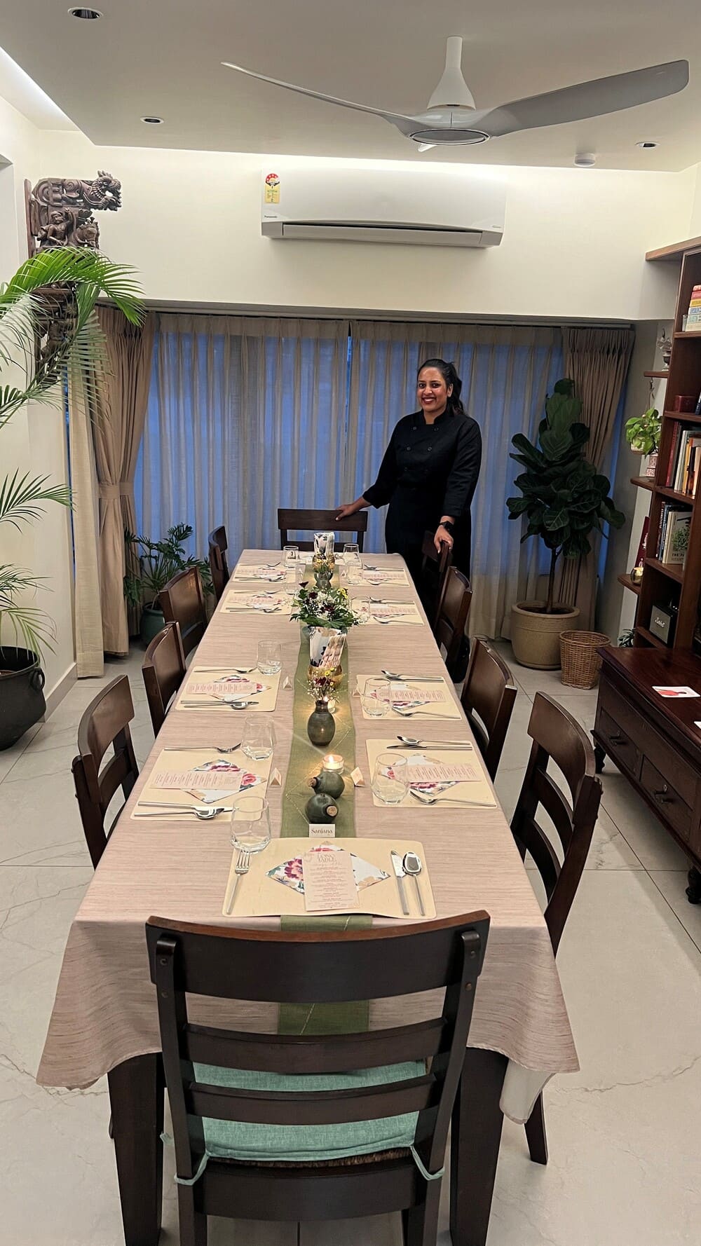 Pragati Mita stands beside dining table covered in tablecloth and dinnerware. 