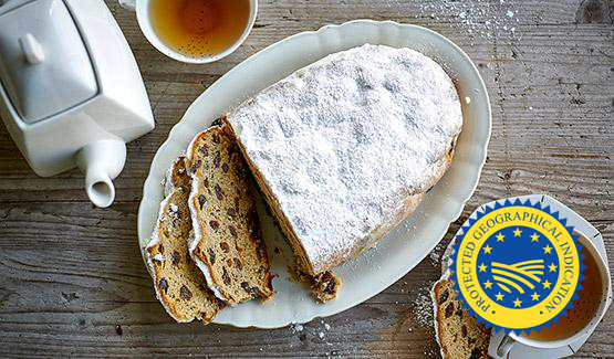 Stollen, an oval bread topped with white flour, sits on a white plate on a wooden table