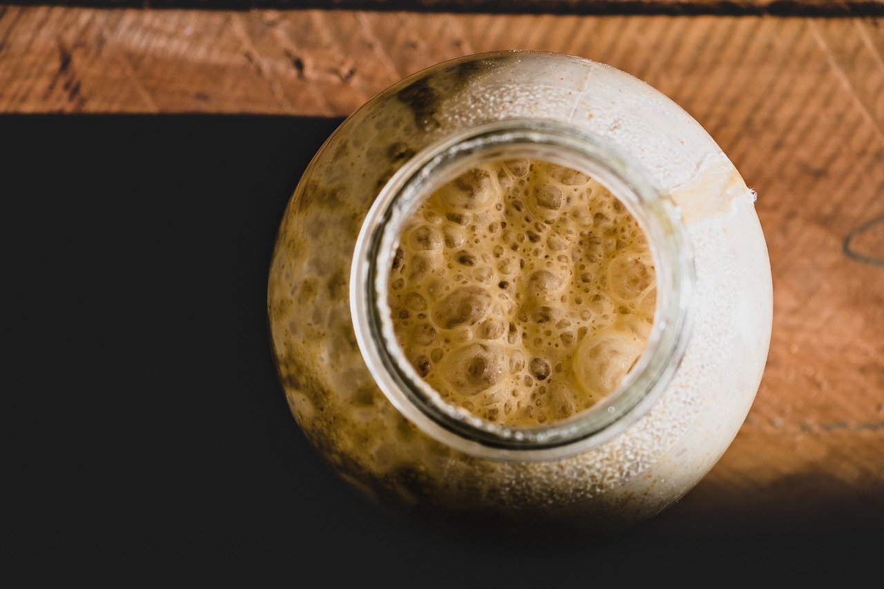 Bird's eye view of bubbling sourdough starter inside glass jar on wood table.