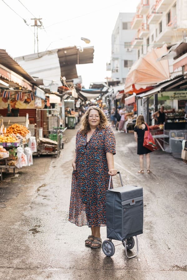 Adeena Sussman at the Jerusalem shuk (outdoor market) wearing a floral dress and standing beside her shopping stroller.