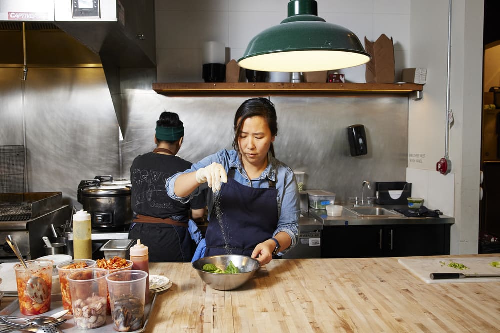 Chef Rachel Yang adds salt to a mixing bowl while making kimchi in kitchen at her restaurant Revel in Seattle.