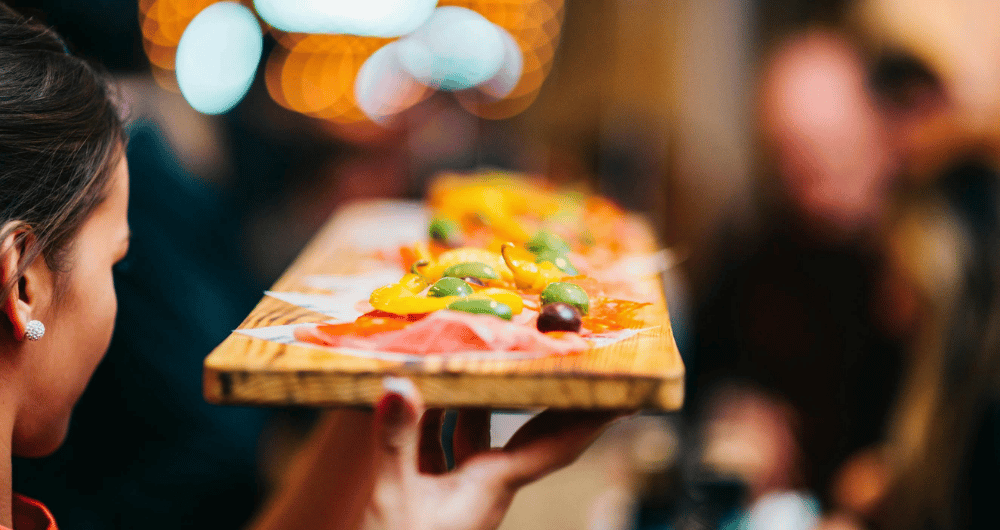 A server at a restaurant holding a wooden tray of appetizers.