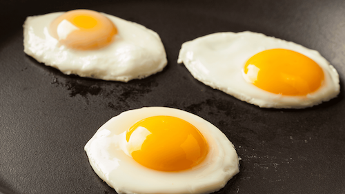 Close-up of three fried eggs in a skillet, showcasing their sunny-side-up appearance and crispy edges.