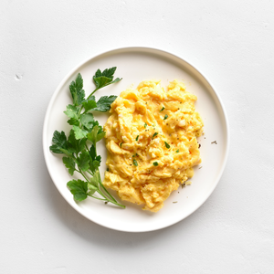 Fluffy scrambled eggs served on a white plate, adorned with parsley for added color and freshness.