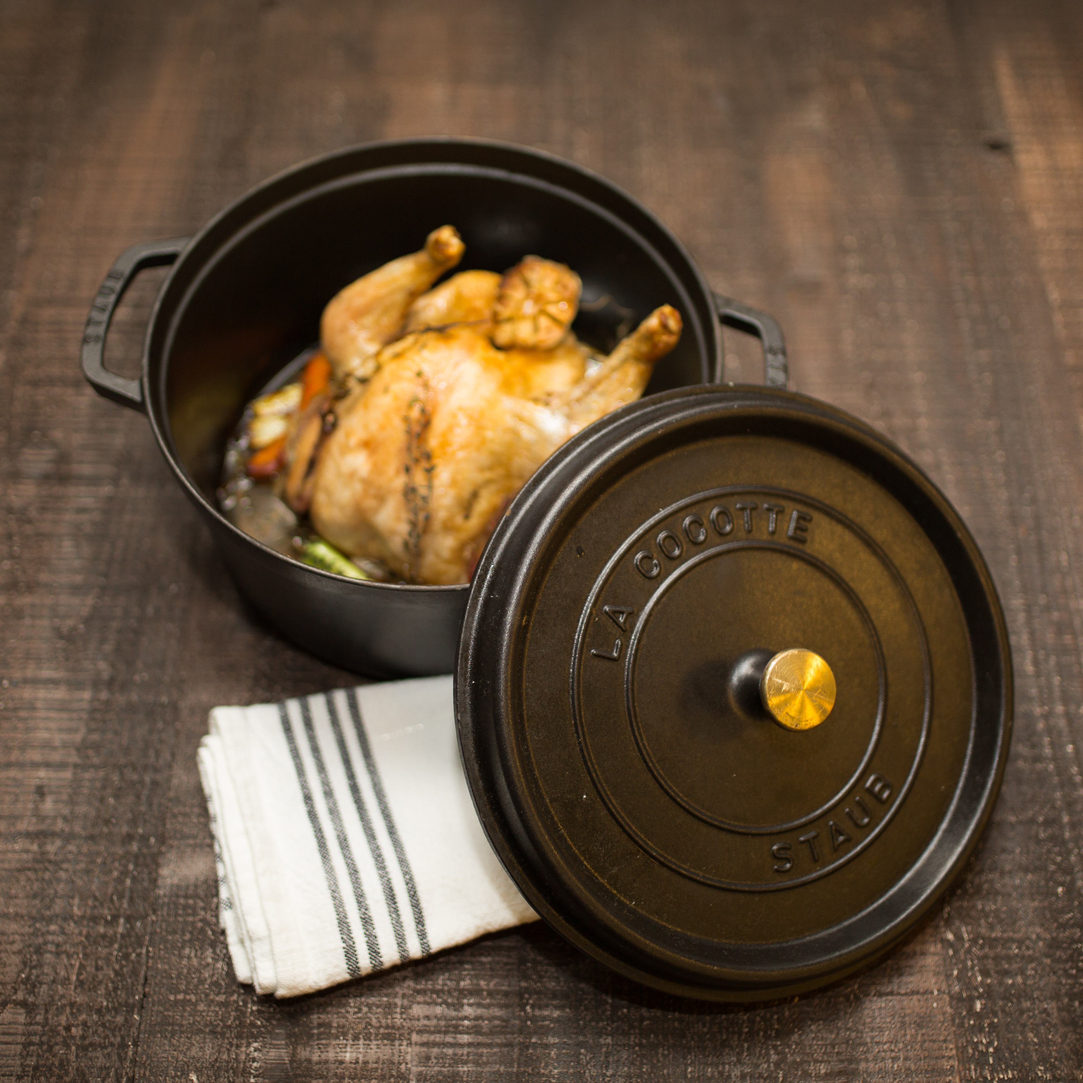 A turkey sits in a black Staub dutch oven on a wooden table