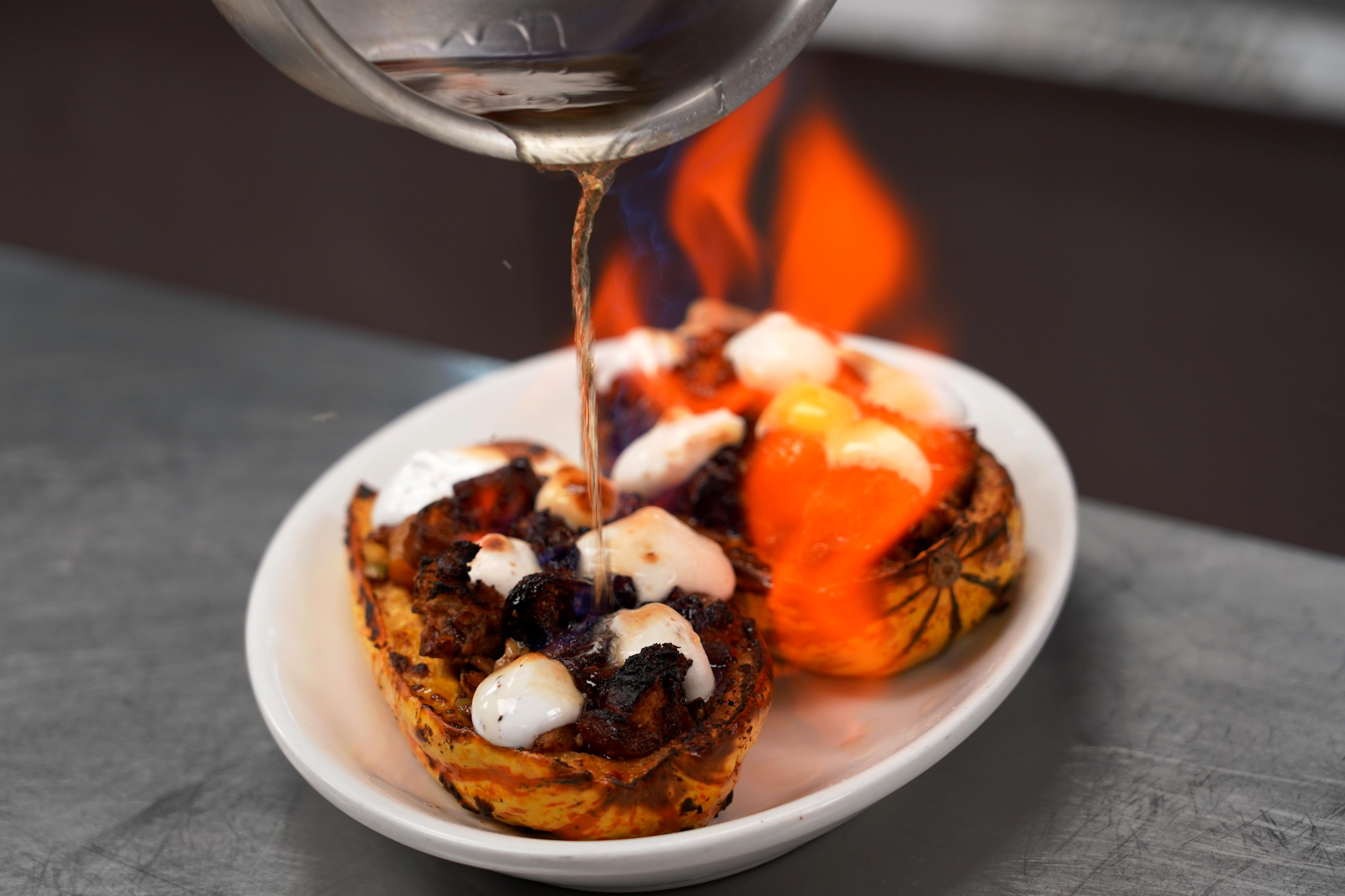 Flaming liquid is poured onto a stuffed squash on a white plate