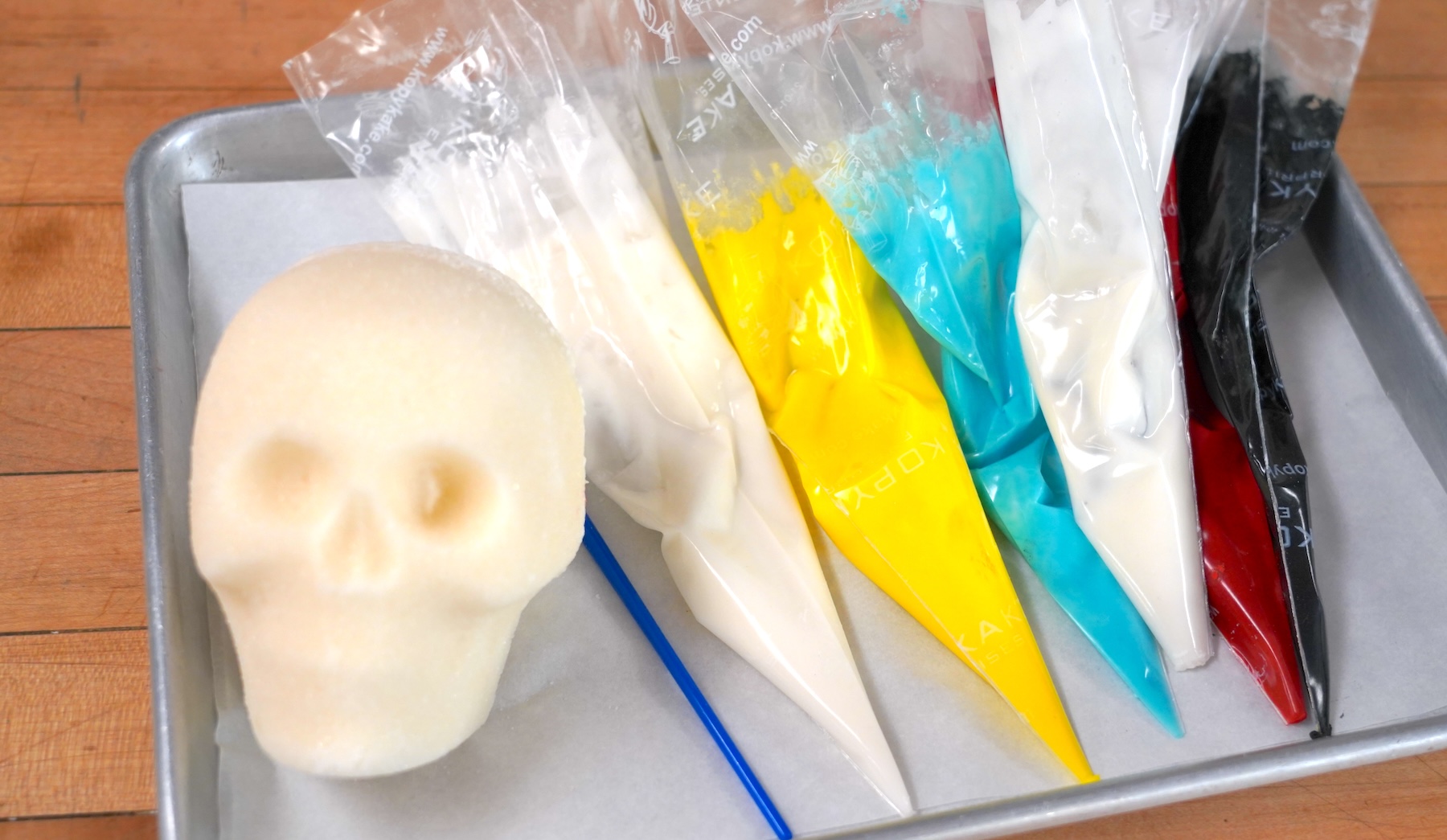 A white sugar skull sits nexts to piping bags full of colored royal icing