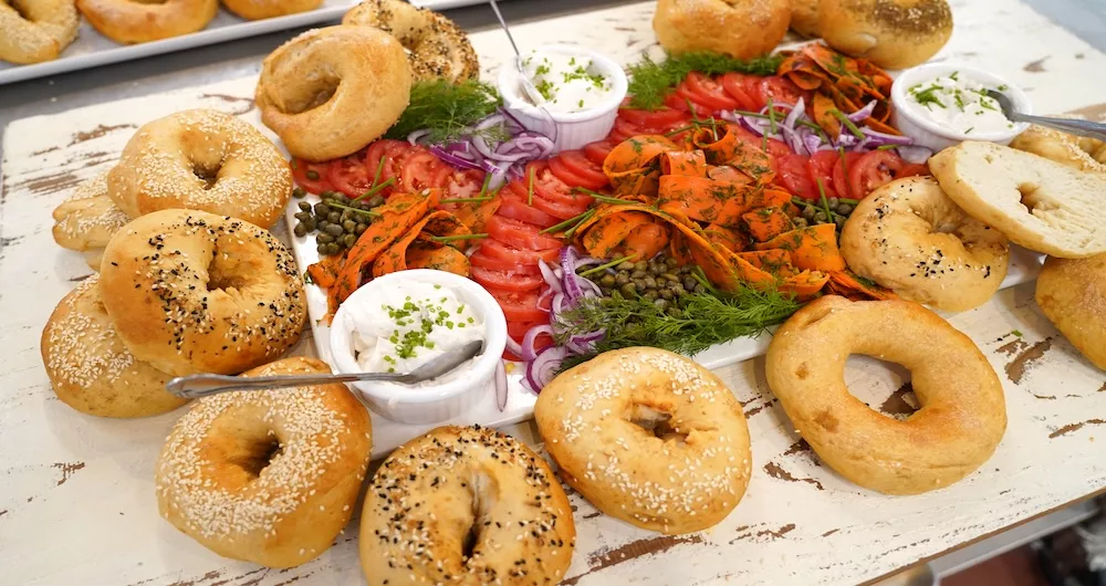 Bagels sit next to a variety of colorful toppings and cream cheese on a white table