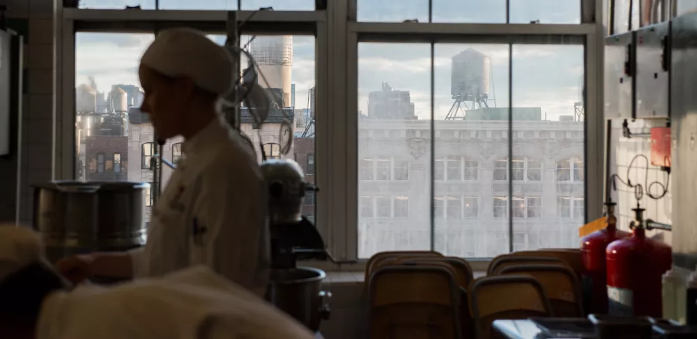 cook walking through a kitchen overlooking manhattan