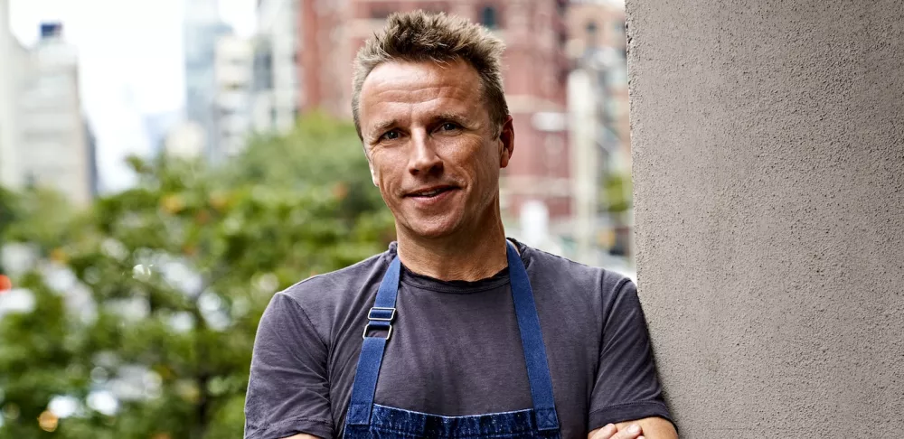 Chef Marc Murphy, a blonde man with a grey shirt and a blue apron, smiles