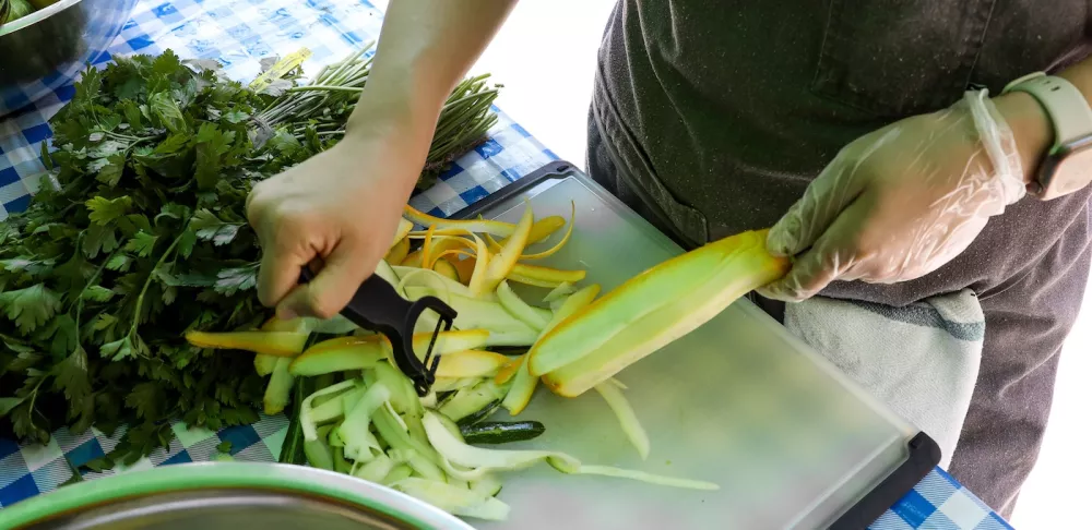 Chef peeling summer squash on a cutting board with herbs in the background