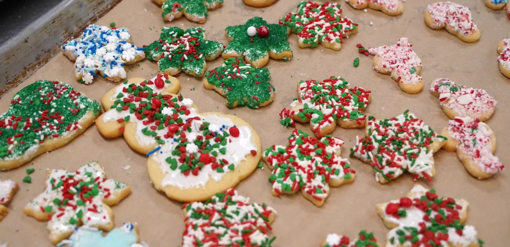 Holiday-themed sugar cookies of various shapes sit on a tray lined with brown parchment paper