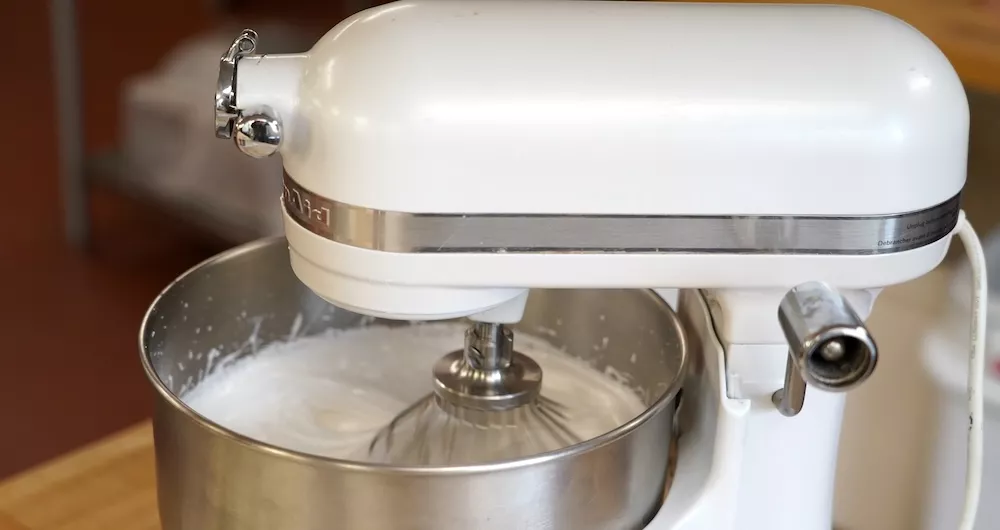 A white KitchenAid stand mixer whipping white buttercream