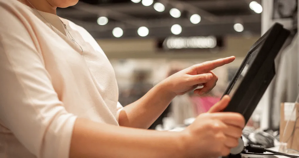Close-up of a person's hand using a point-of-sale touchscreen monitor while holding a paper receipt.