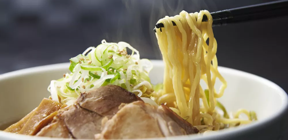 Chopsticks pull ramen noodles out of a bowl of soup