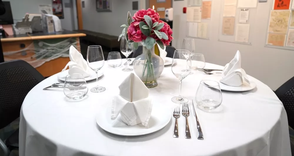 A set table with white tablecloth and red flowers in a vase