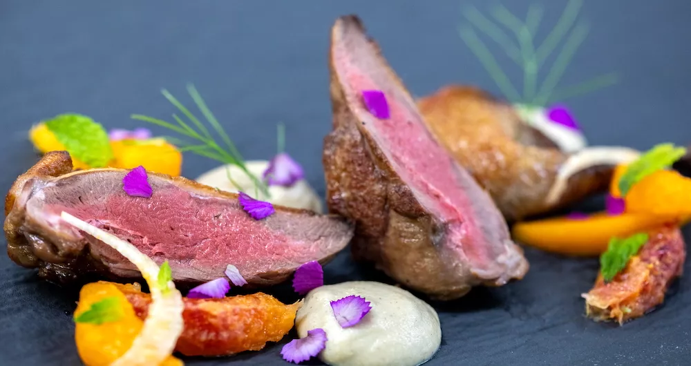 Pieces of steak, vegetables and cream sauce on a black plate