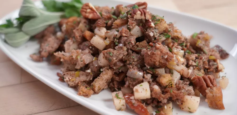 Stuffing sits on a white plate next to green herbs