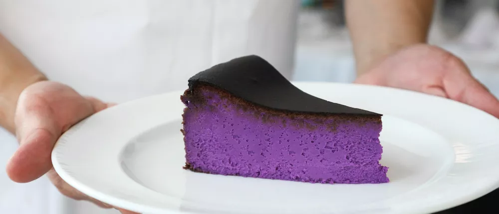 Purple ube Basque cheesecake on a white plate, chef hands on the plate