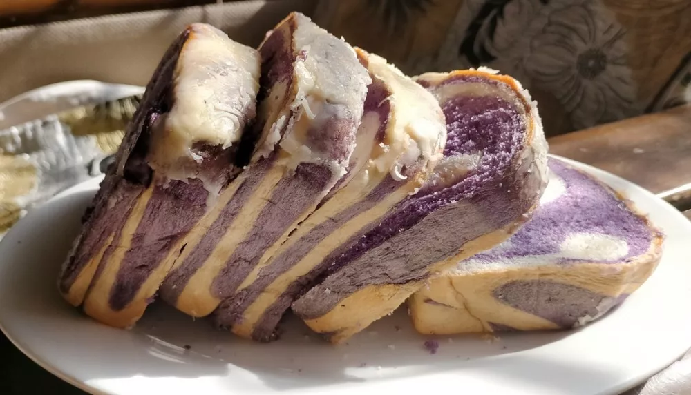 5 thick slices of purple swirled ube bread sit on a white plate.