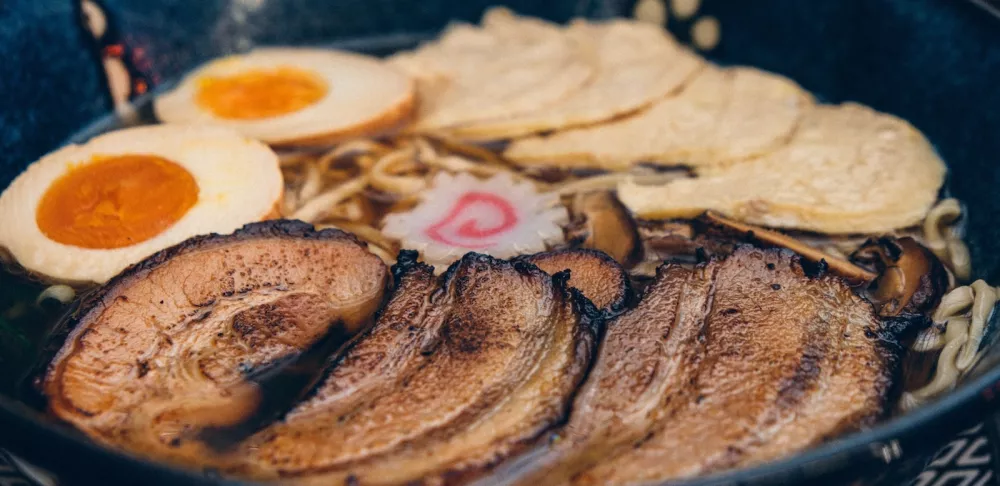 Meat, noodles and egg in ramen broth in a blue bowl