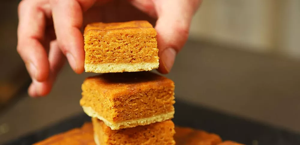 a hand places an orange pumpkin blondie bar on a stack of blondies