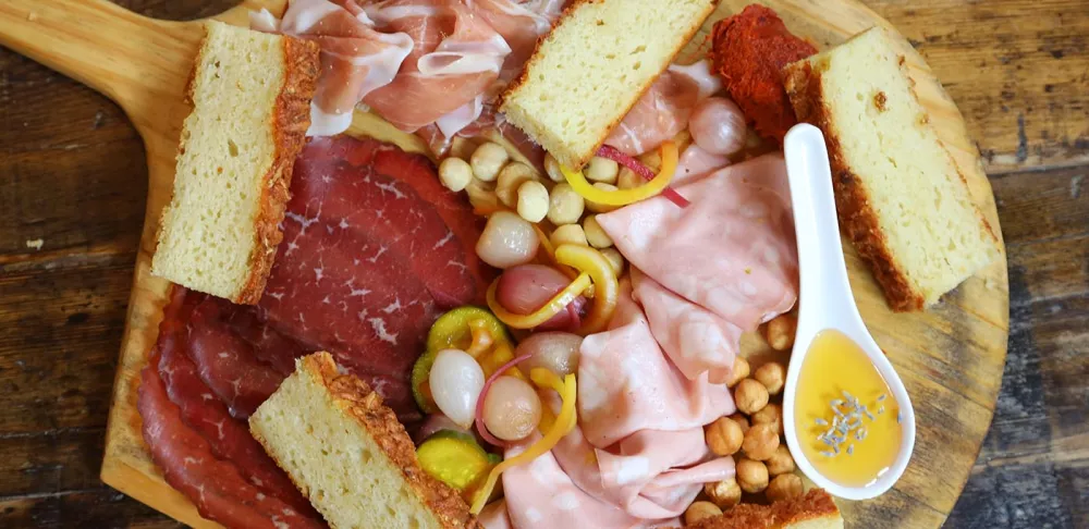 Assorted charcuterie meats, vegetables and bread sit on a brown board