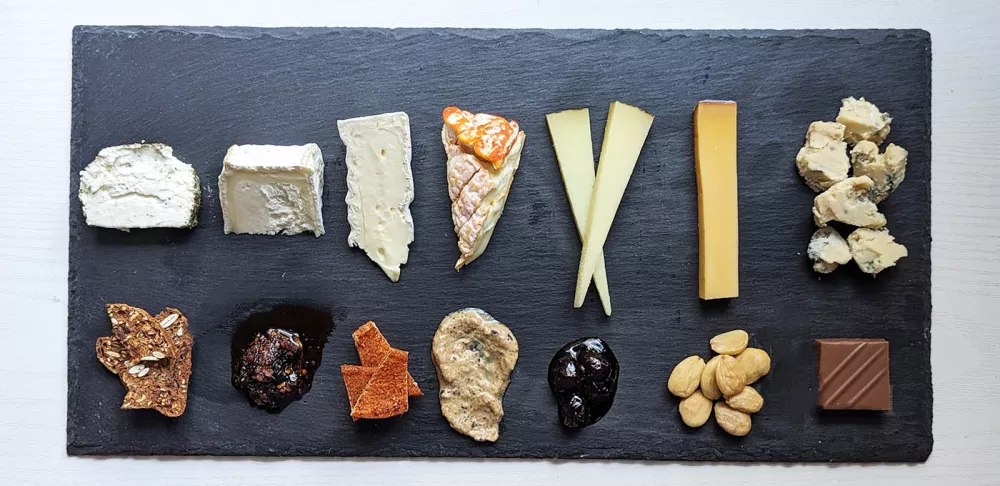 Multiple types of cheese a fruit sit on a black stone board