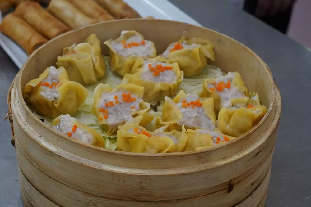 A dozen colorful gyoza sit on a bed of lettuce in a bamboo steamer. 