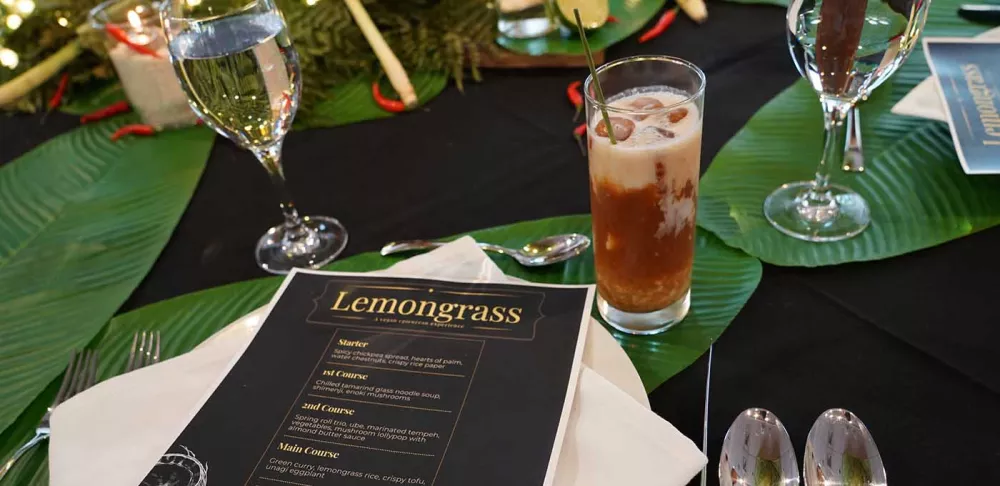 A black restaurant menu with white text sits on a table surrounded by silverware and drinks