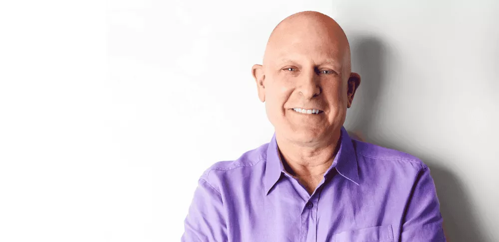 Picture of Chef Elliot Prag in purple collared shirt standing in front of white wall